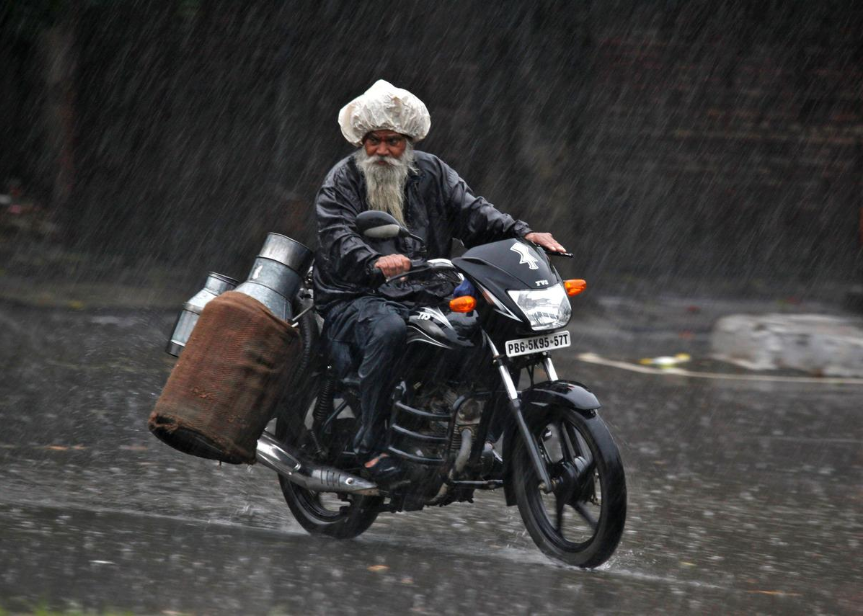 Milkman rides motorcycle in monsoon