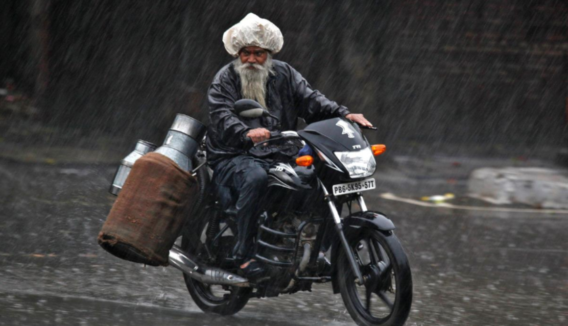 Milkman rides motorcycle in monsoon